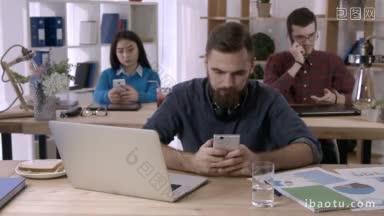 满脸胡须的商人在开放的办公室里用手机浏览社交网络，而多民族的同事则忙着玩智能手机